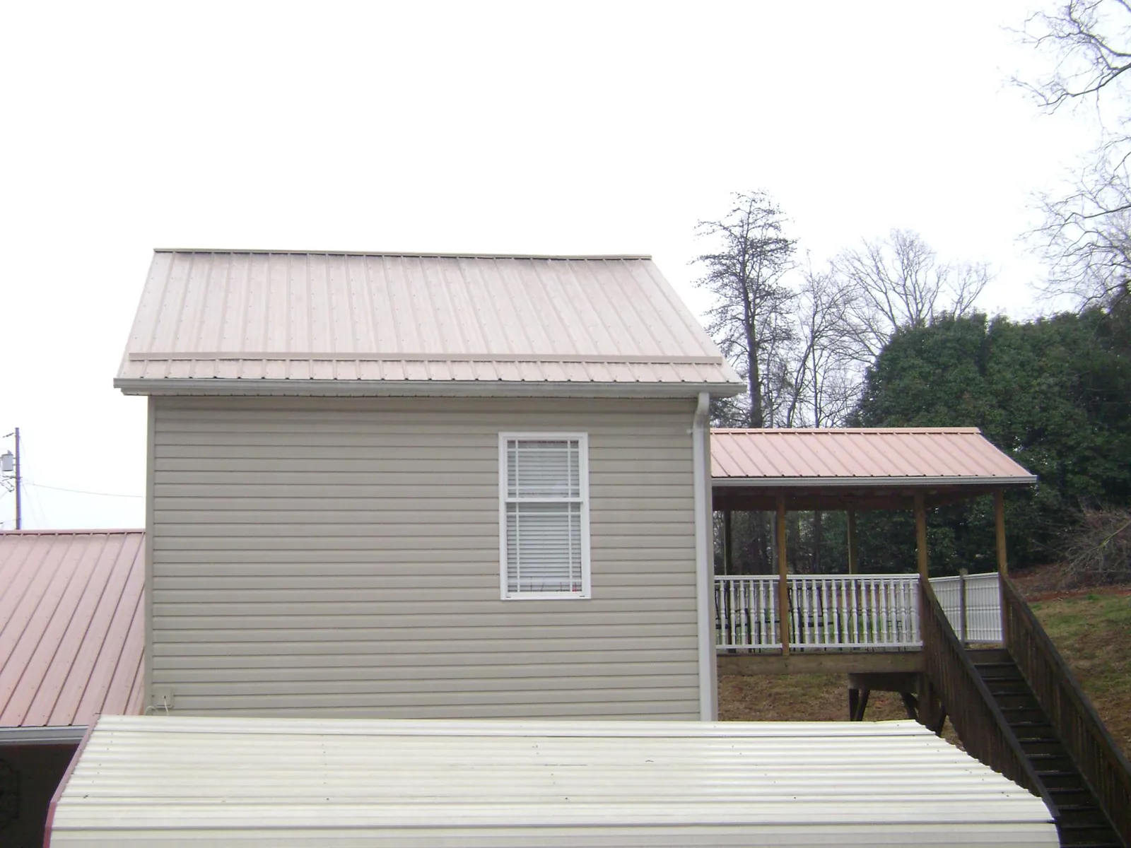 Tan metal roofs on a two story addition and attached porch, from a Roof Replacement job in Merrill