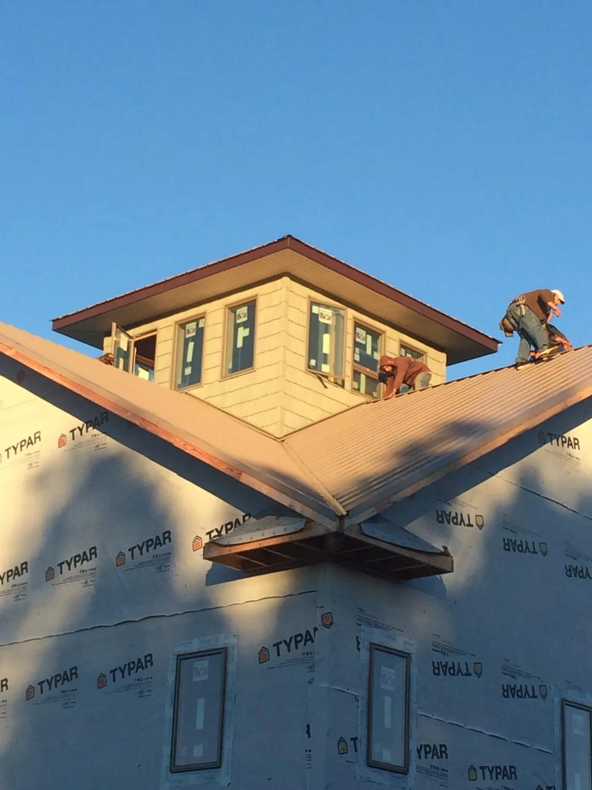 Roofers working around a rooftop cupola on a new metal roof at sunset — Roof Waterproofing in Merrill by Roofing Brothers